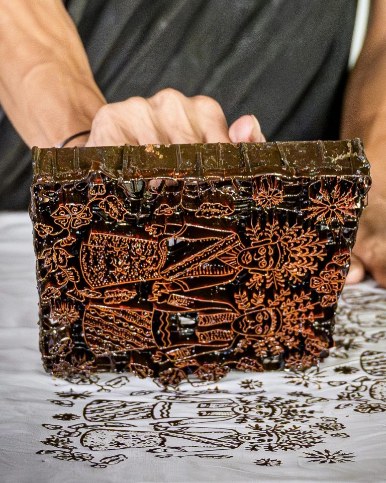 Close-up of a craftsman using a wooden block for batik printing in Jakarta.